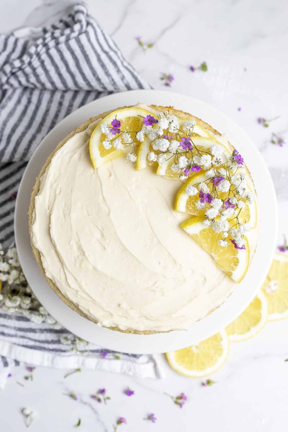 Cake topped with lemon buttercream frosting, sliced lemons and flowers.