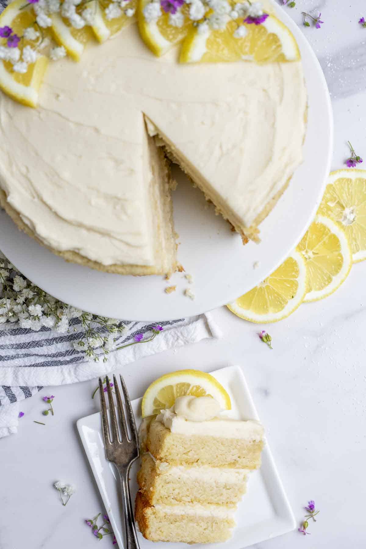 slice of lemon cake with lemon grossing on a plate with the rest of the cake in the background.