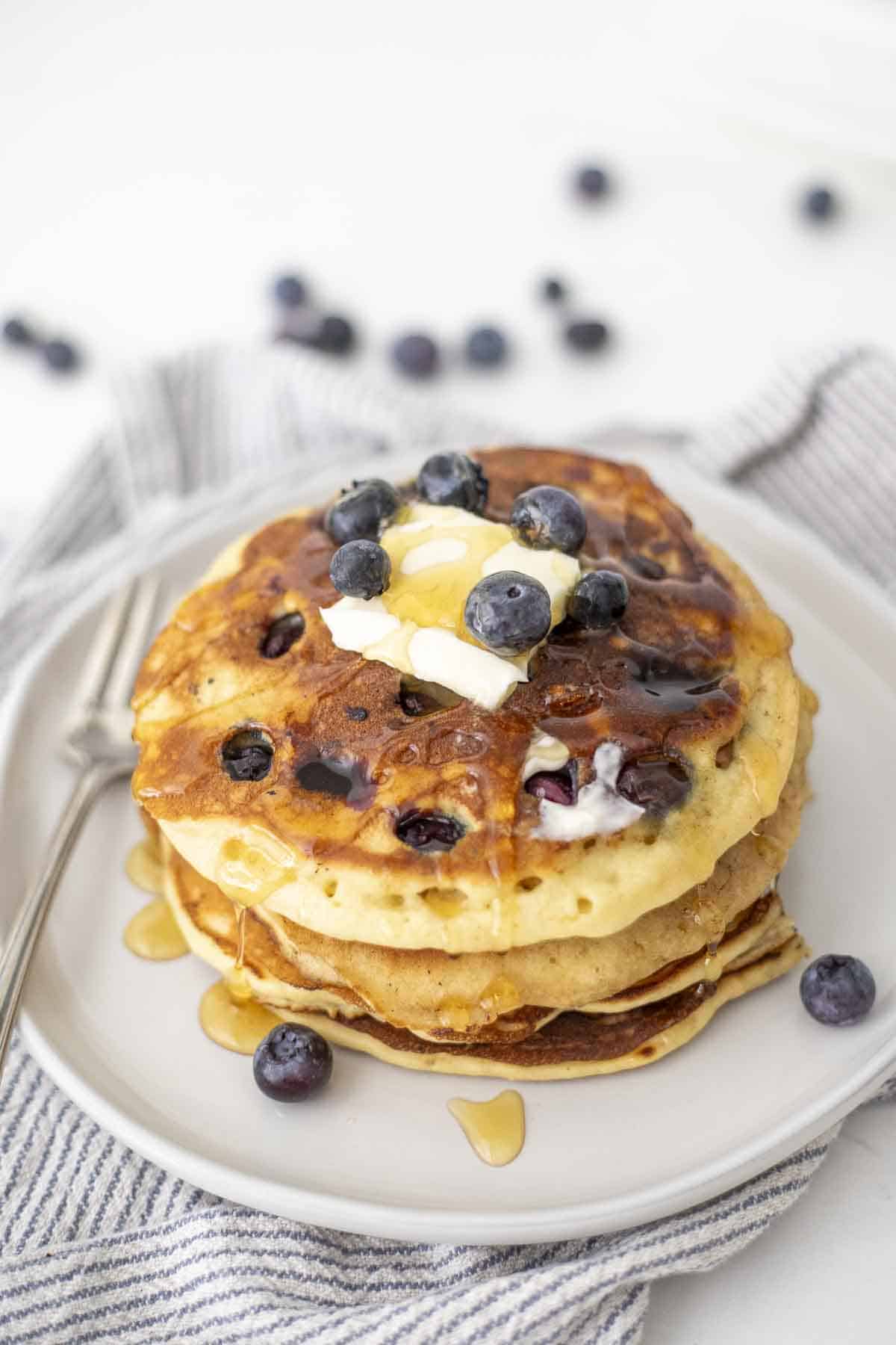 a stack of sourdough blueberry pancakes with a pat of butter and honey on top. The pancakes are on a white plate.