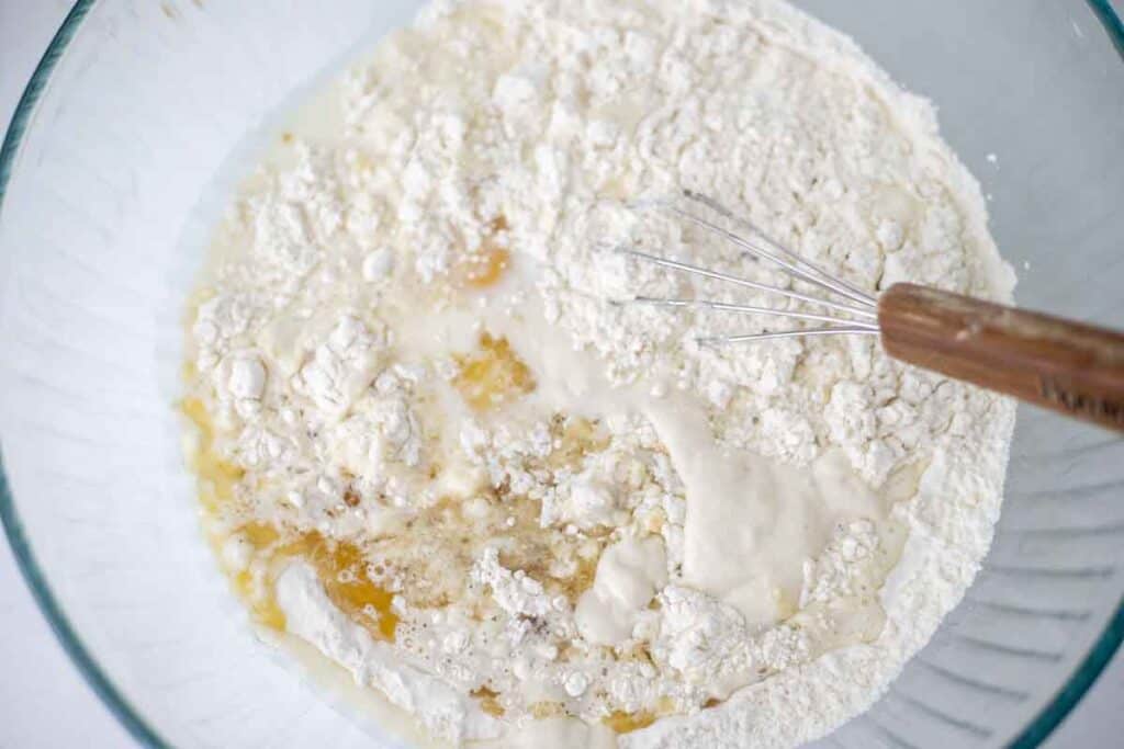 Adding milk, melted butter, sourdough starter, and egg to the dry ingredients in a bowl.