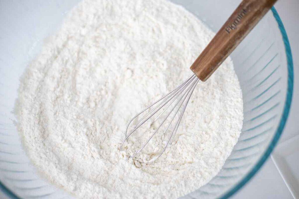 Dry ingredients in a glass bowl with a whisk.