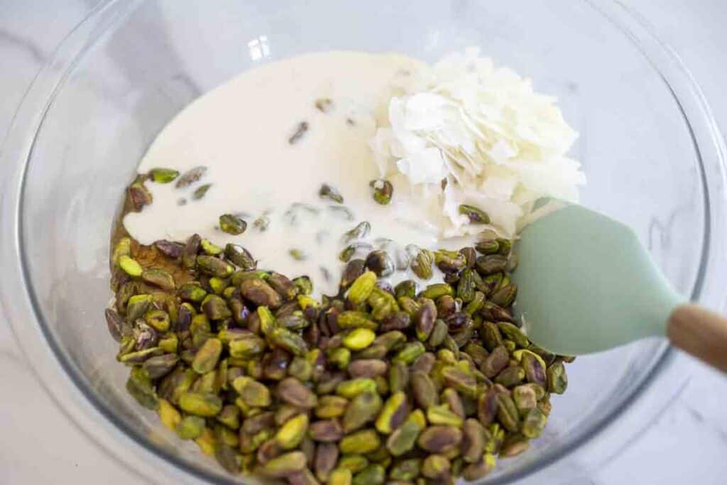 sourdough starter and honey added to nuts and oats in glass bowl.