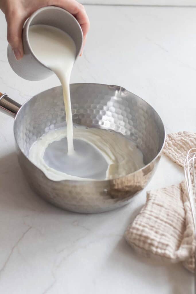 Milk being poured into a silver saucepan.