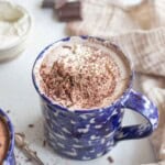 A blue mug filled with hot chocolate, topped with whipped cream and chocolate shavings.