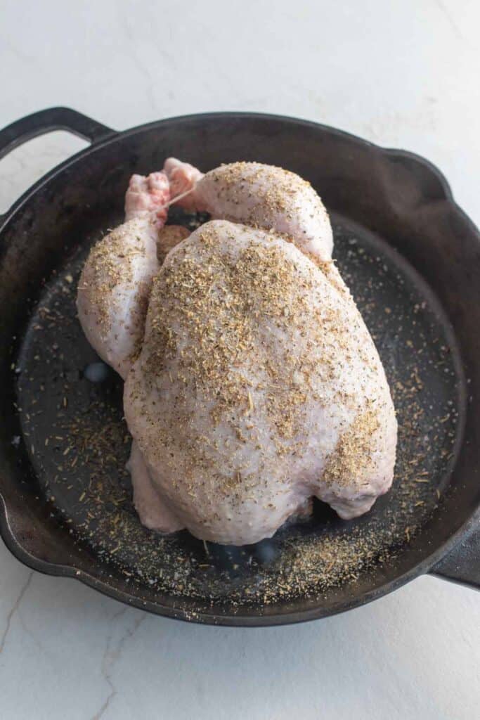 A whole chicken in a cast iron skillet oiled and seasoned.