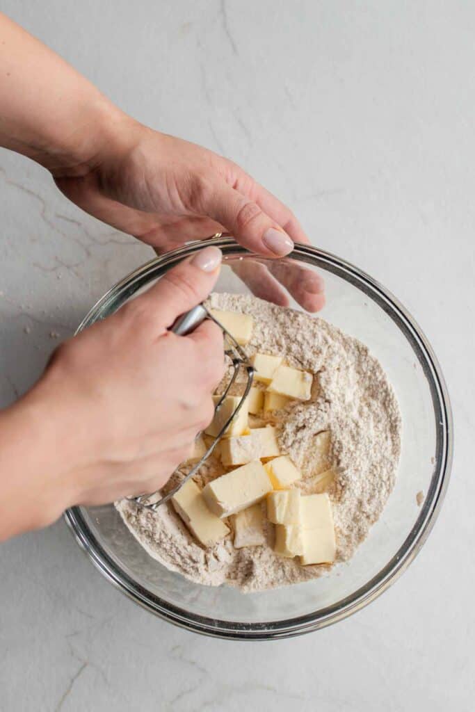 Someone using a pastry cutter to cut cold chunks of butter into the dry ingredients.