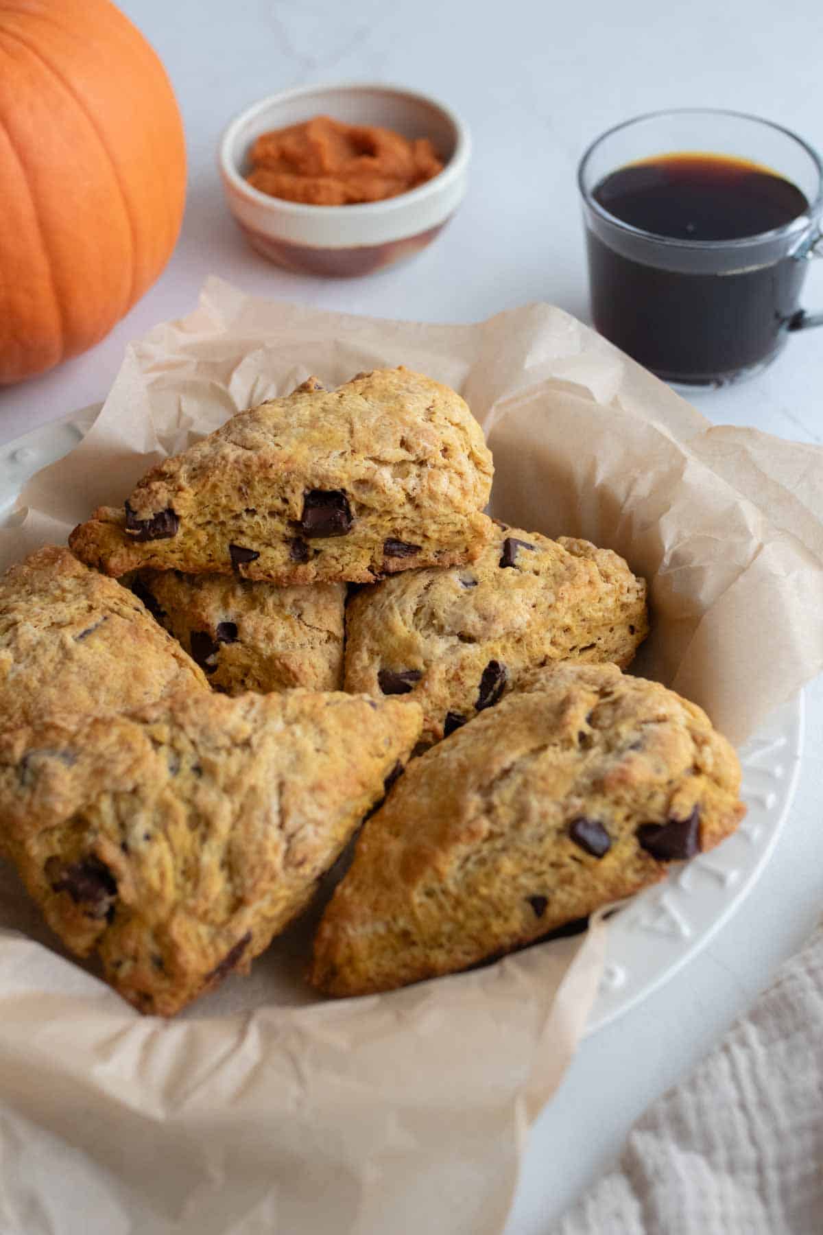 A bowl of pumpkin scones with coffee and a pumpkin in the background.