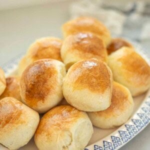 Sourdough brioche rolls stacked up on a blue and white plate.