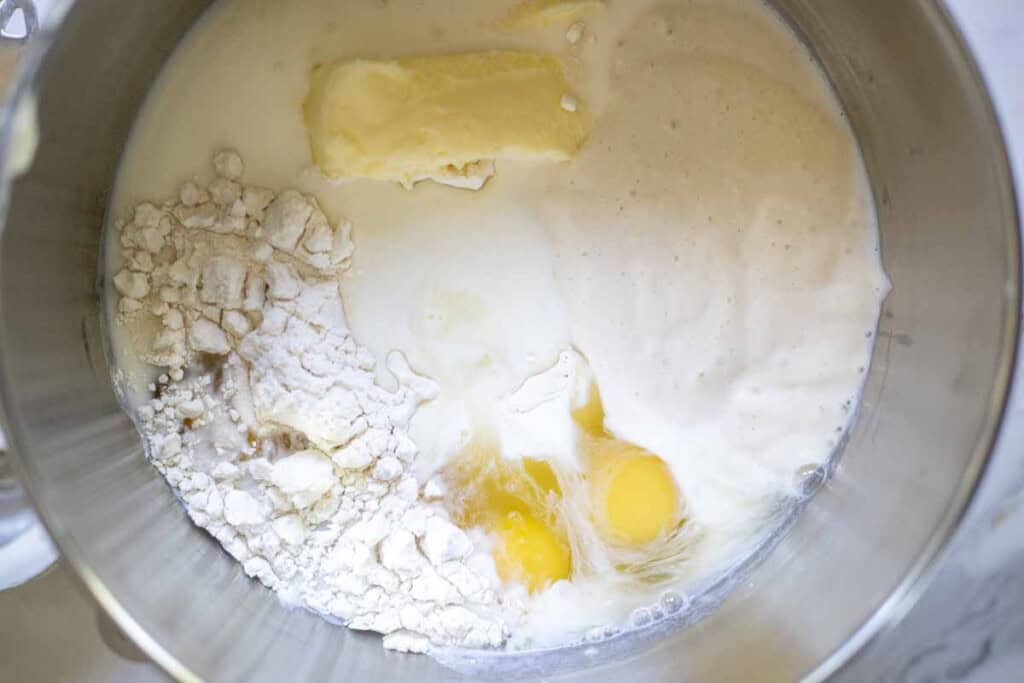 Flour, sourdough starter, butter, milk, eggs and other ingredients in a stand mixer bowl.