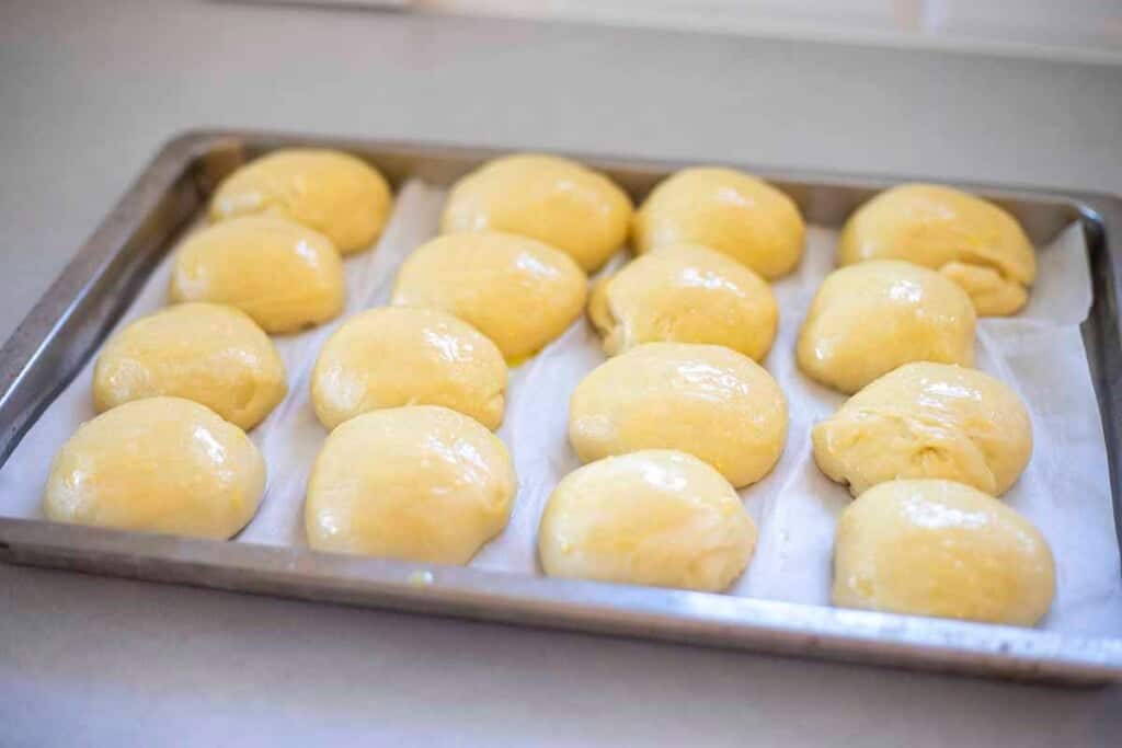 Risen rolls brushed with an egg wash on a parchment lined baking sheet.