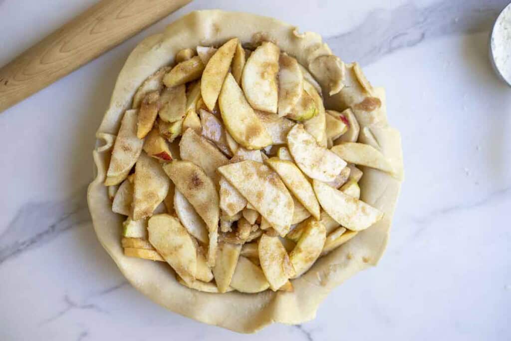 apple pie filling in a pie dish with a rolled out pie dough.