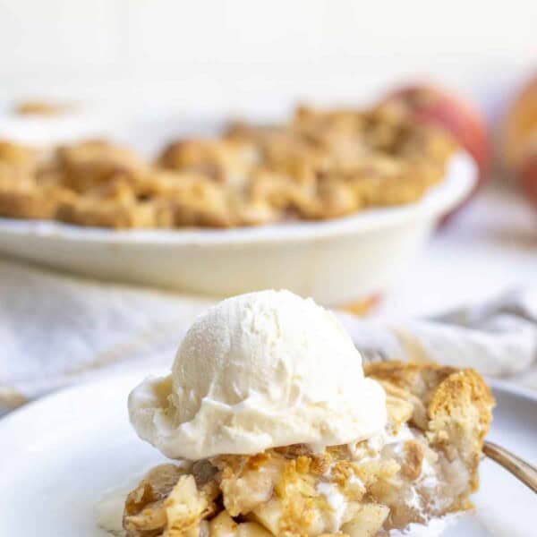 slice of apple pie topped with a scoop of ice cream on a white plate. More pie is in the background.