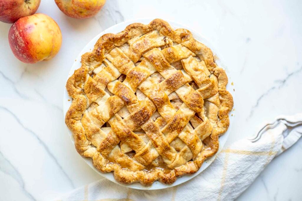 overhead photo of a baked apple pie. Apples and a napkin are next to the pie.