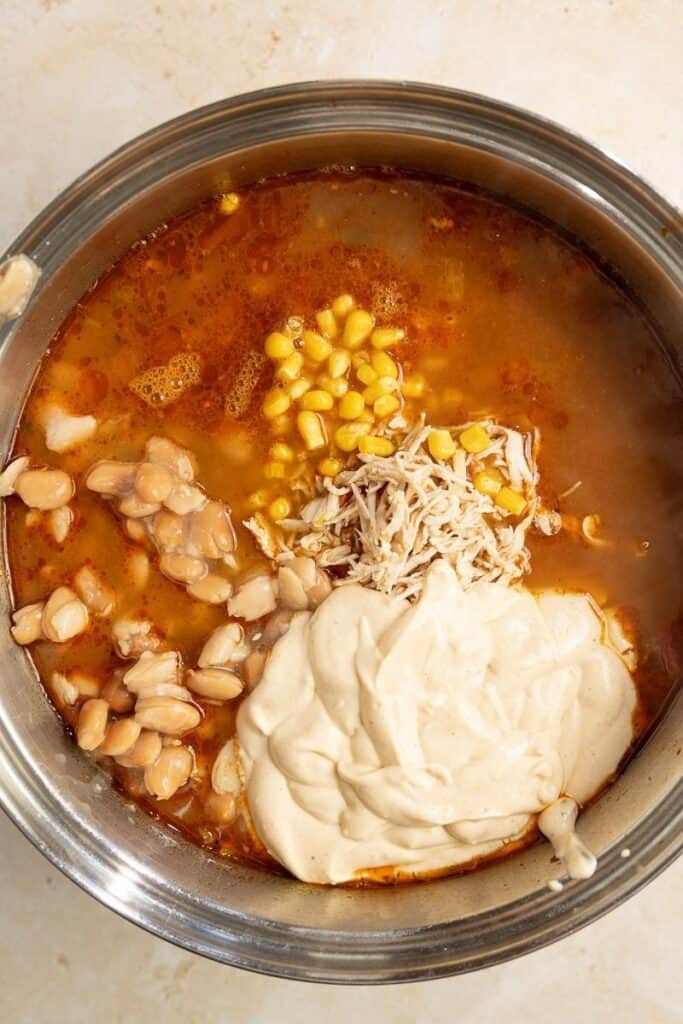 A large stock pot filled with broth, beans, corn, and cream cheese.