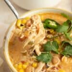 A bowl of white chicken chili with a spoon picking up a big bite.