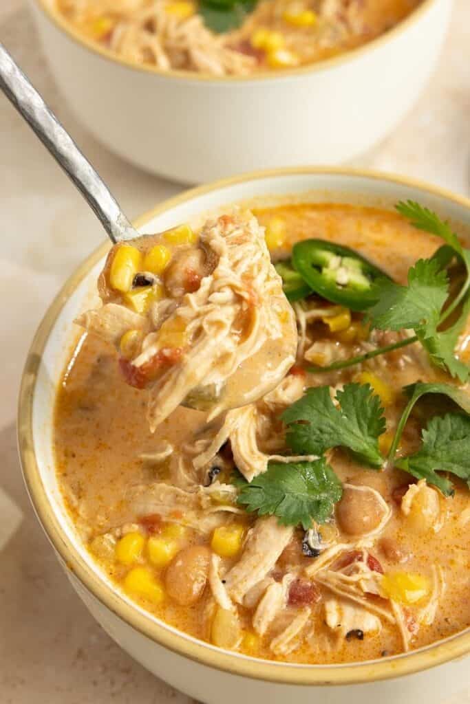 A bowl of white chicken chili with a spoon picking up a big bite.