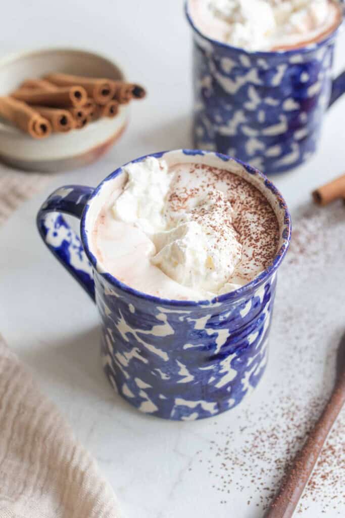 Two mugs filled with hot chocolate and topped with whipped cream.