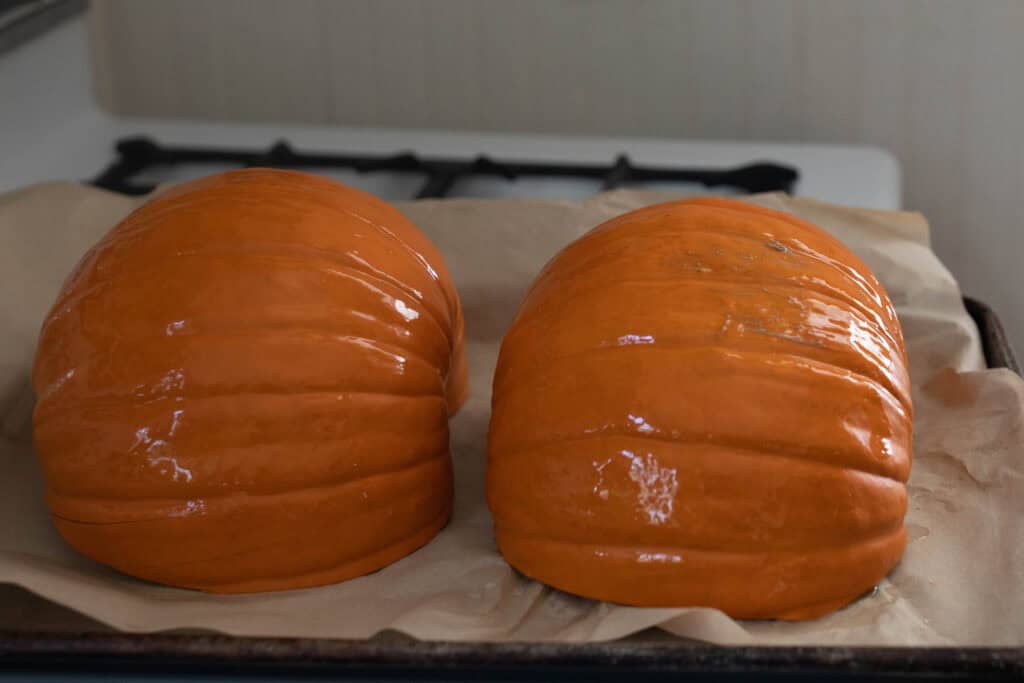 Two halves of a pie pumpkin placed on a parchment paper lined baking sheet. 