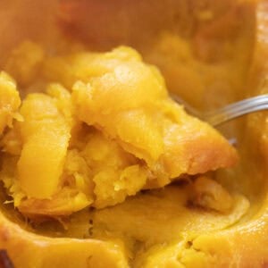 A spoon scooping out the inside of a roasted pie pumpkin.