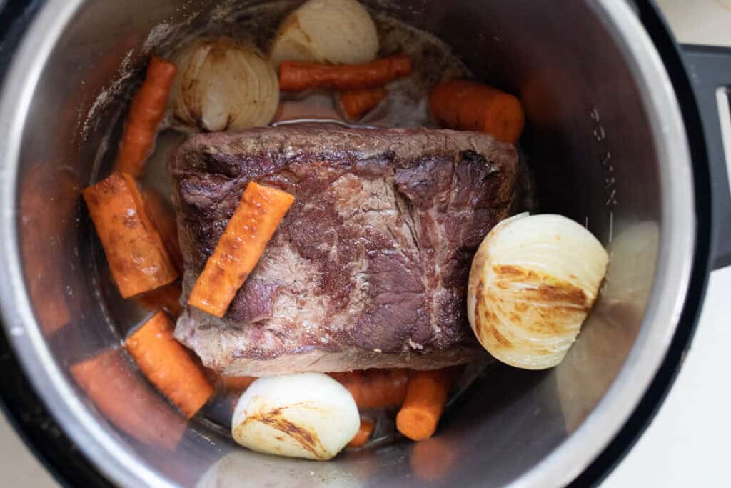 A chuck roast with onions and carrots in an Instant Pot.