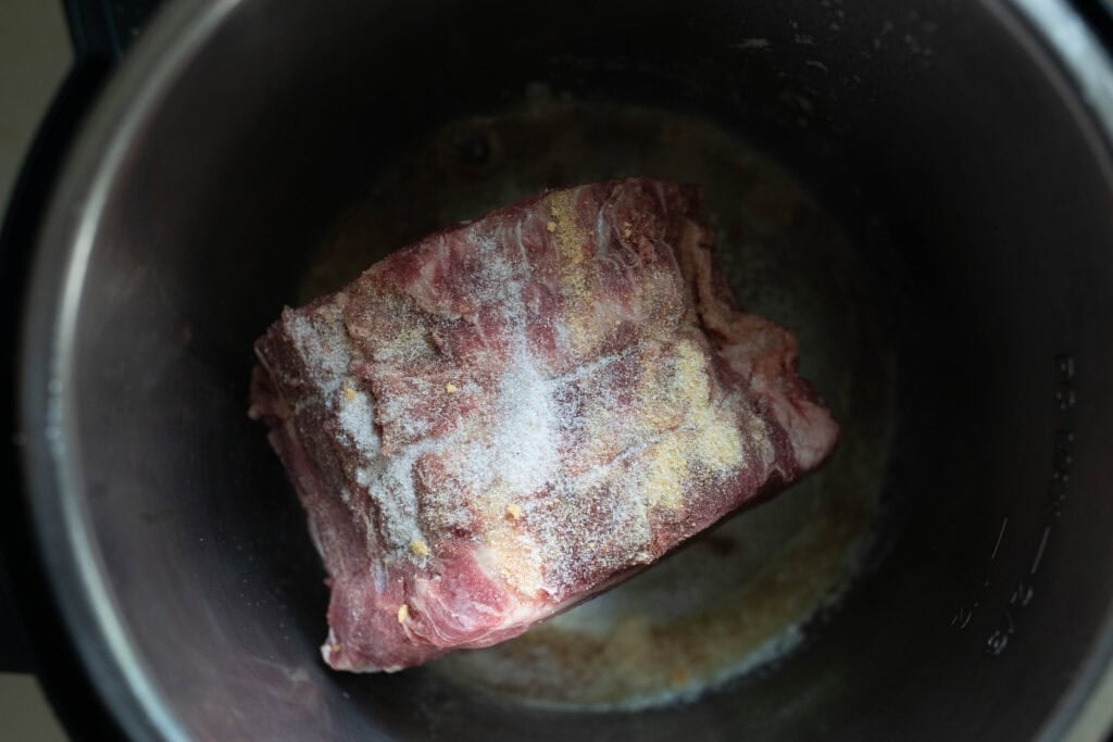 A chuck roast sprinkled with salt, garlic powder, and pepper in an Instant Pot.