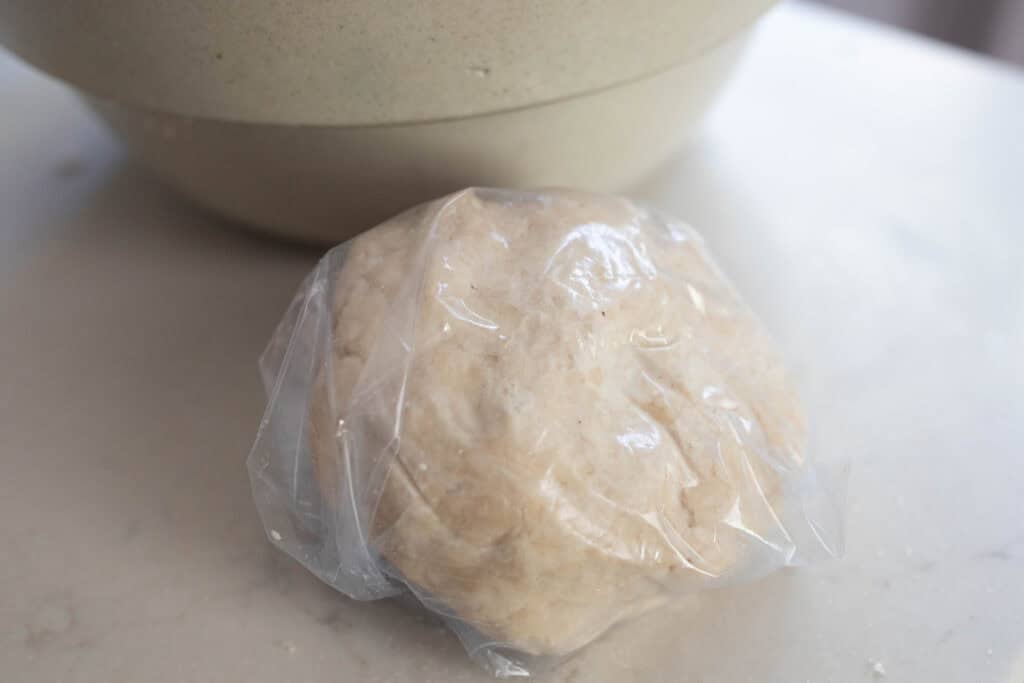 Pie dough in a bowl wrapped in plastic wrap.