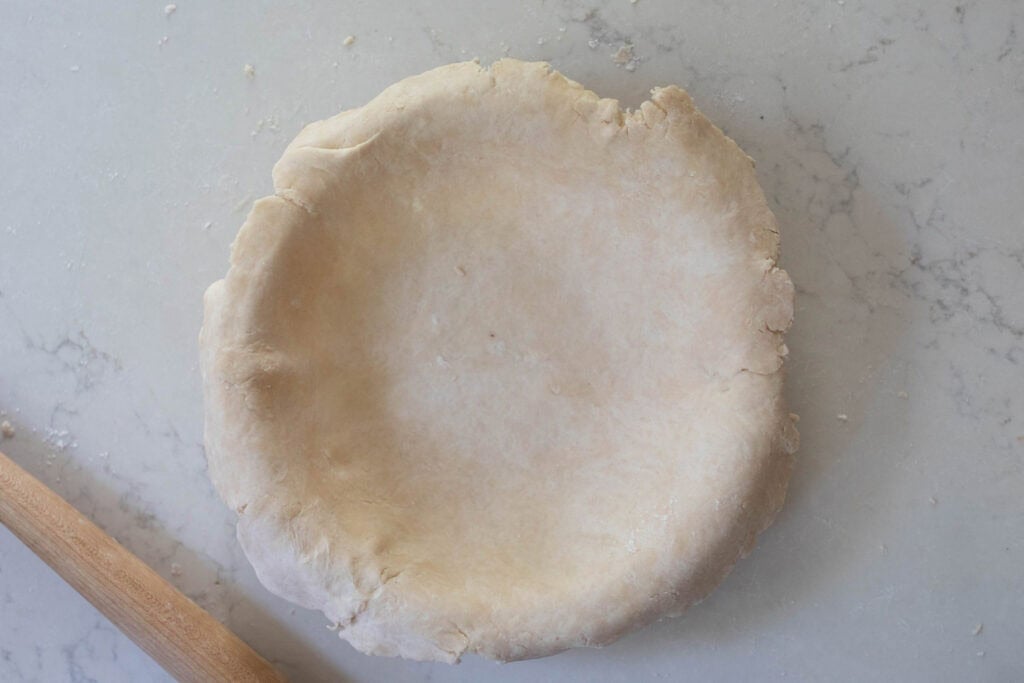 Pie dough rolled out and laying over a pie pan.