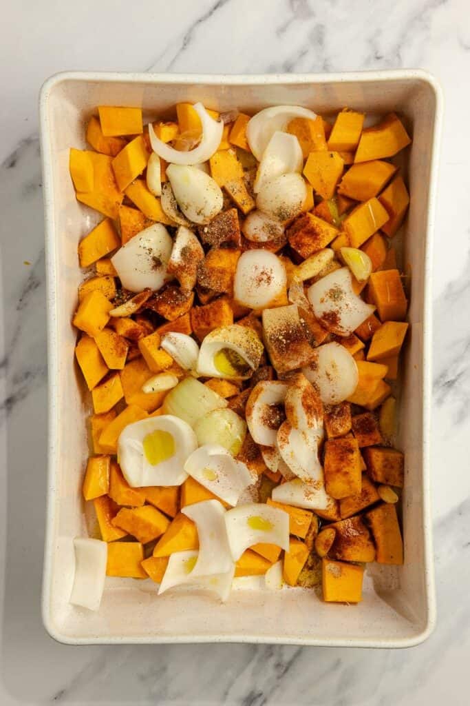 Onion and pumpkin cut up into chunks in a baking dish and seasoned.