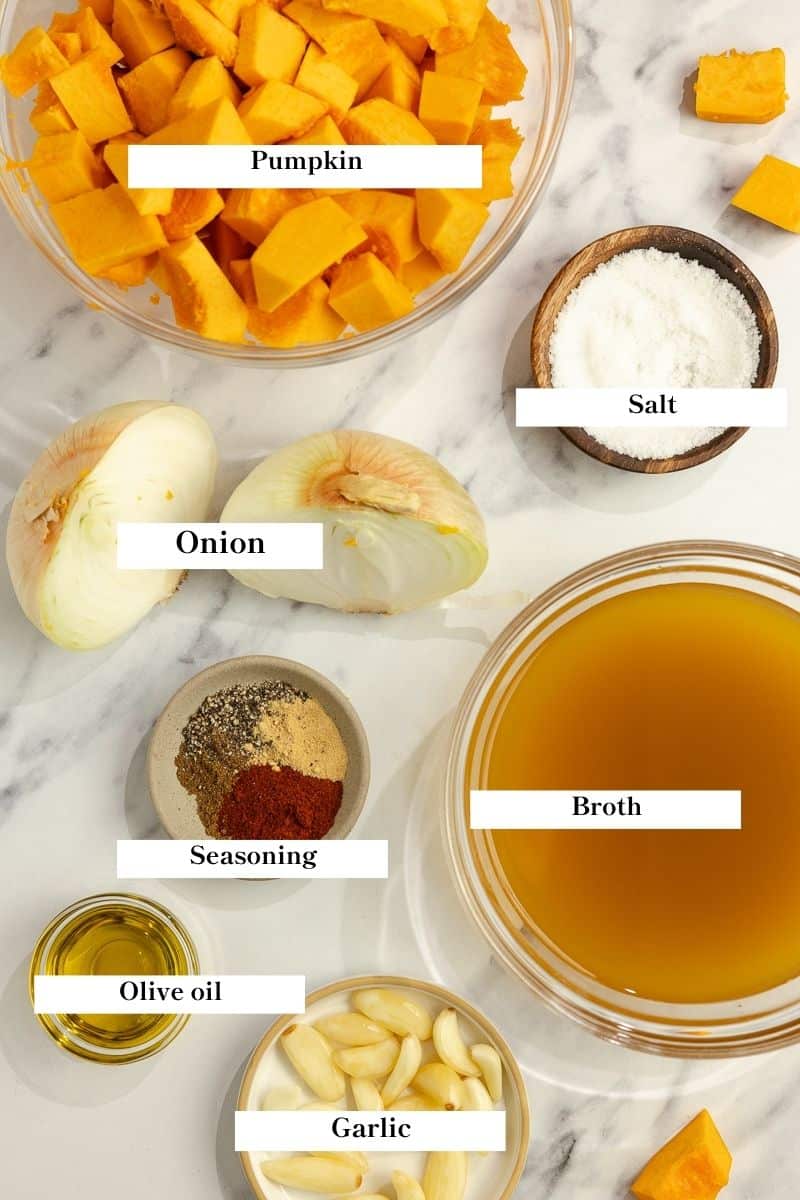 Ingredients for pumpkin soup laid out on a white countertop.