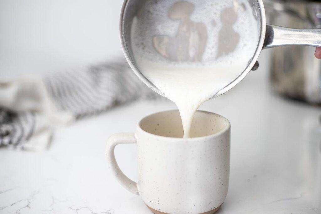 Pouring frothed milk over rooibos tea in a mug.