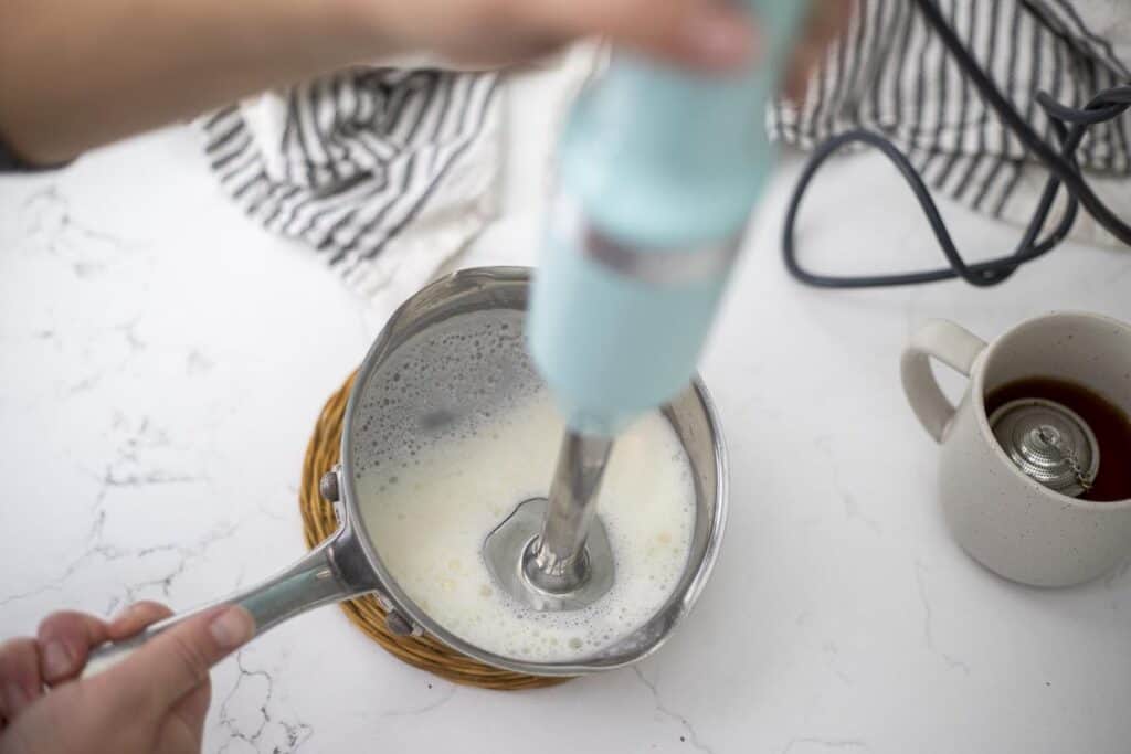 Frothing milk in a small saucepan with an immersion blender.