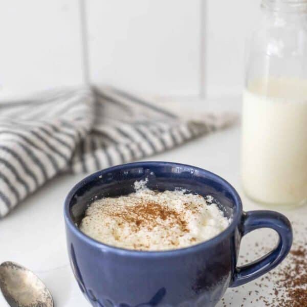 blue mug of rooibos latte topped with cinnamon on a white countertop with ingredients surrounding the mug.