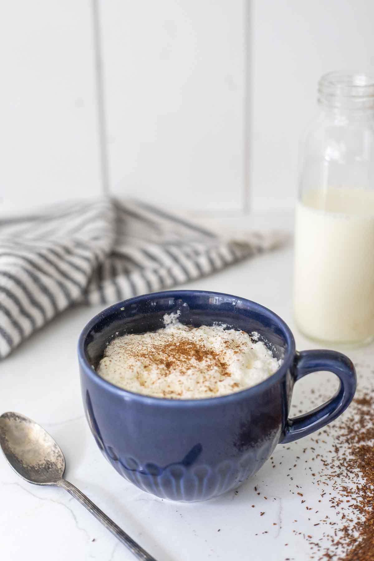 blue mug of rooibos latte topped with cinnamon on a white countertop with ingredients surrounding the mug.