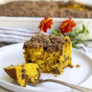 A slice of pumpkin coffee cake with a bite on a fork on a white plate.