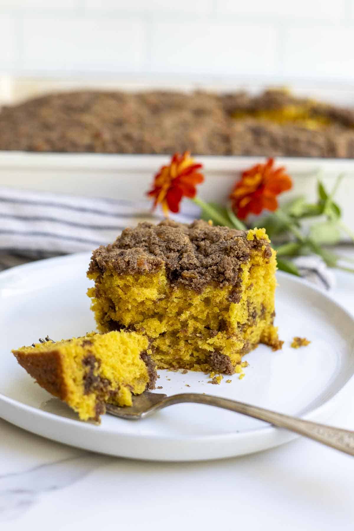 A slice of pumpkin coffee cake with a bite on a fork on a white plate.