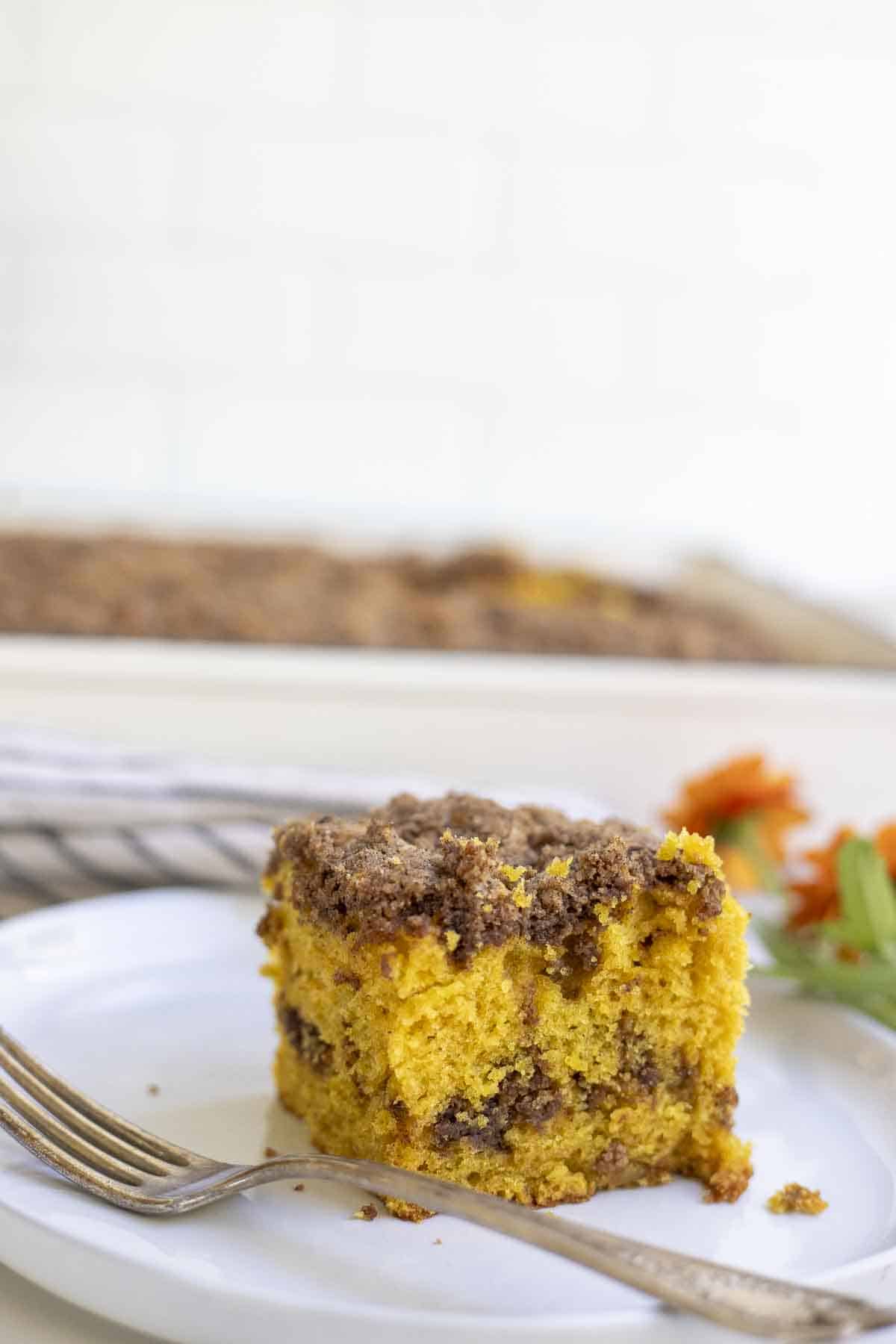 slice of sourdough pumpkin coffee cake on a white plate with a fork. More cake is in the background.