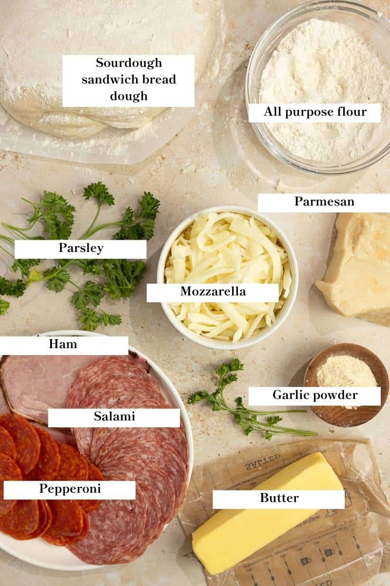 Bread dough, cheese, butter, meats, and other ingredients on a countertop.