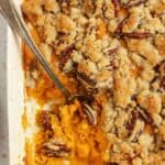 Sweet potato casserole in a baking dish with a serving missing and a big silver spoon.