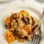 A small white plate with a serving of sweet potato casserole on it with a silver fork.