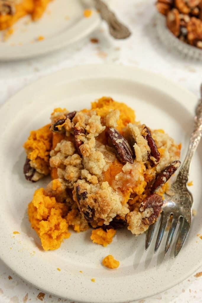 A small white plate with a serving of sweet potato casserole on it with a silver fork.