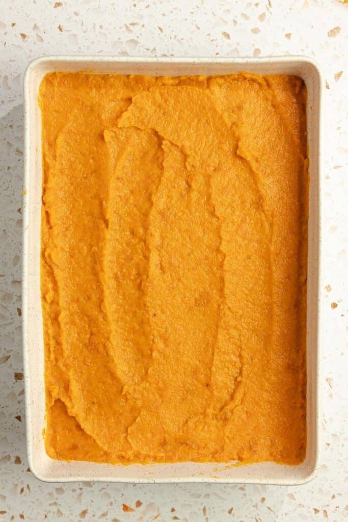 A casserole dish with sweet potato casserole filling spread evenly in it. 