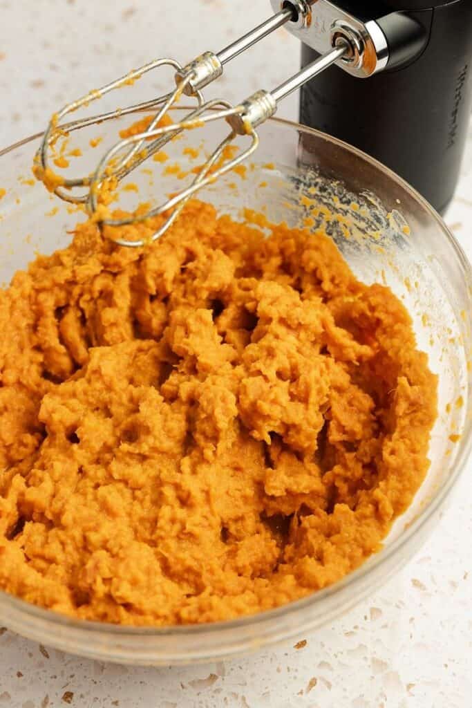 Sweet potatoes mixed with a hand mixer in a large mixing bowl with heavy cream and other ingredients.