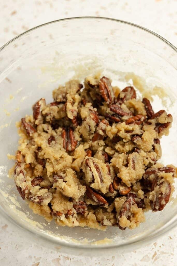 Pecans in a clear bowl mixed with brown sugar and other ingredients.