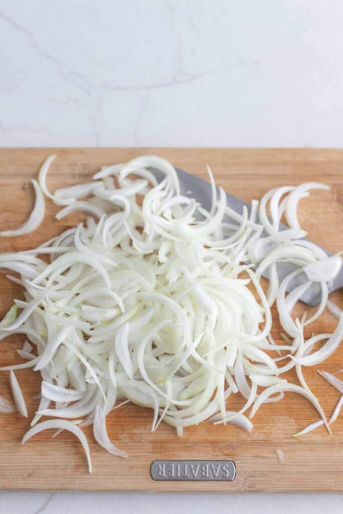 An onion sliced thinly on a wooden cutting board.