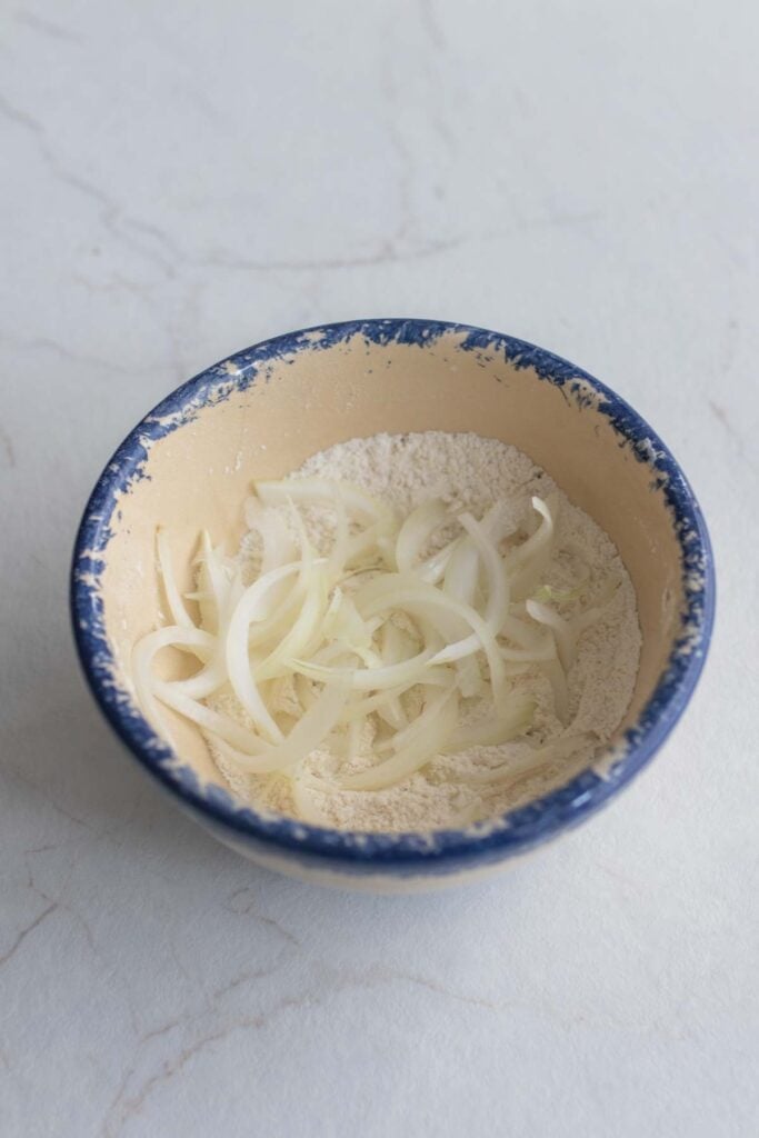 Sliced onions in a bowl with seasoning. 