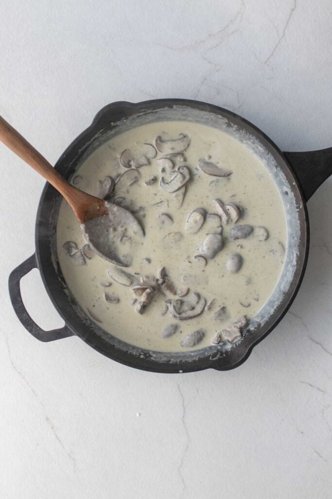 Sliced mushrooms in a heavy cream sauce in a cast iron skillet.