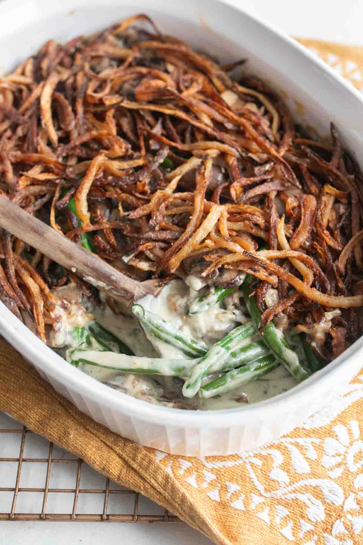 A casserole dish filled with green bean casserole with a wooden spoon scooping out a serving.