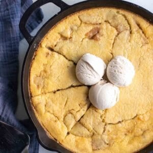 A cast iron skillet with sourdough apple cobbler topped with three scoops of ice cream.