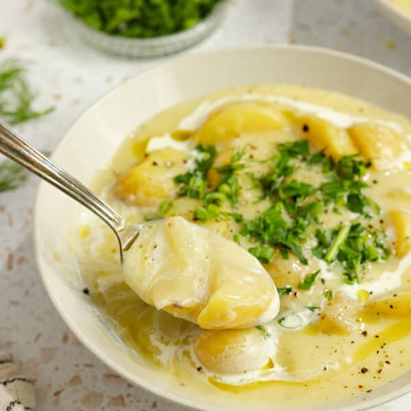 hearty bowl of potato soup topped with fresh herbs in a bowl with a spoonful of soup over the bowl.