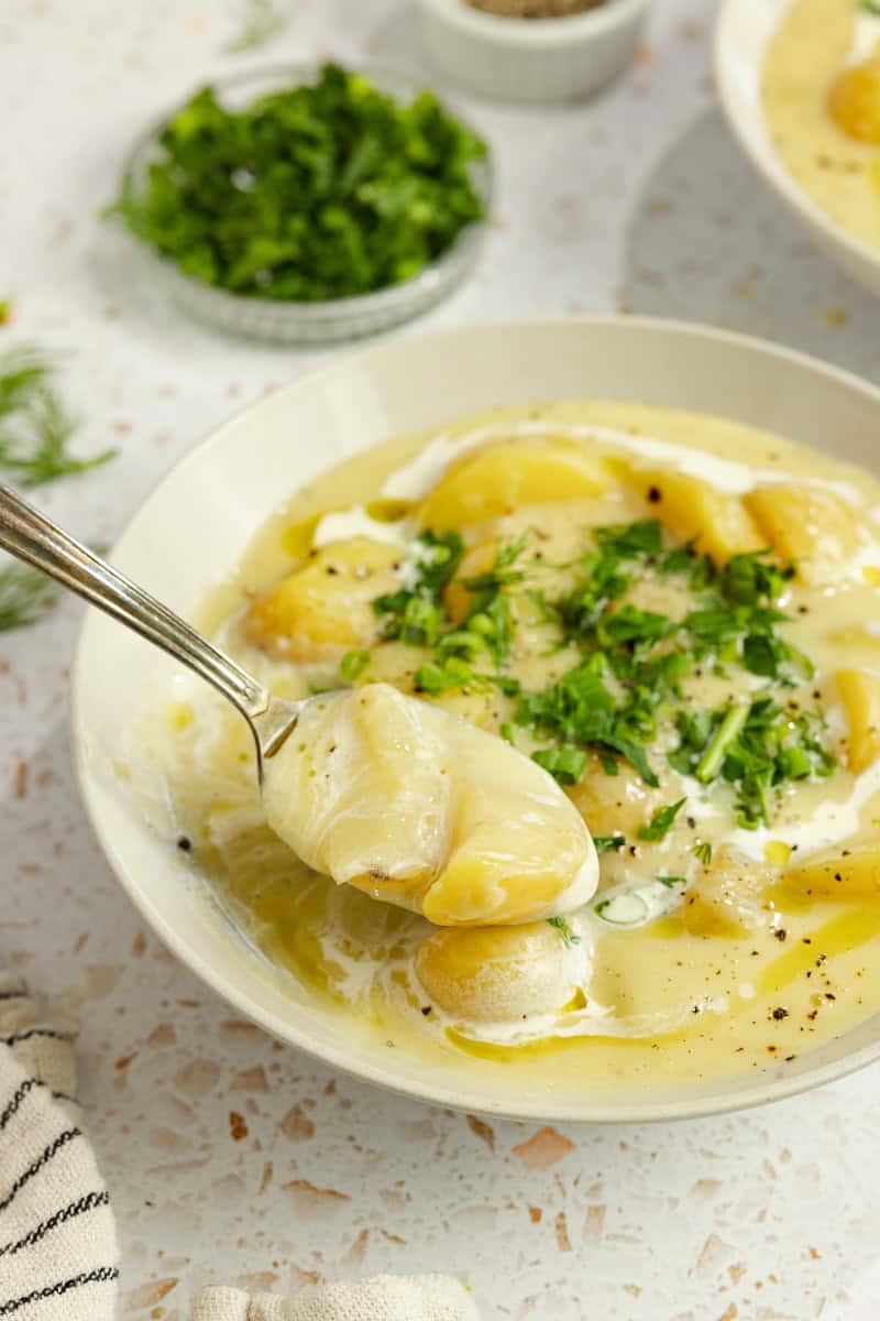 hearty bowl of potato soup topped with fresh herbs in a bowl with a spoonful of soup over the bowl.